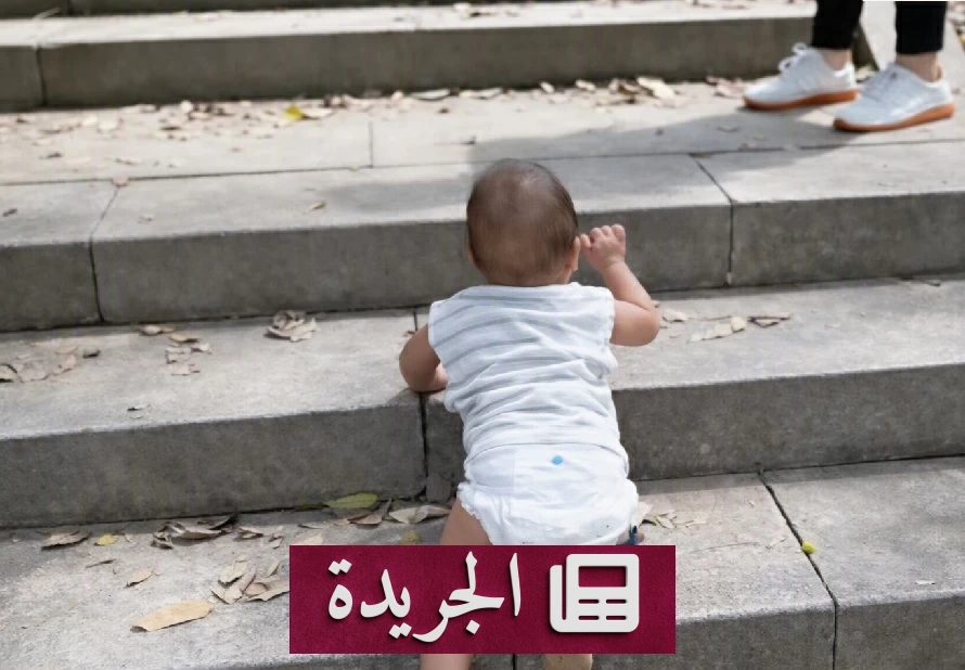 طفل صيني صغير يرتدي واقيات للركبتين أثناء تسلقه درجات جبل تحت مراقبة والدته